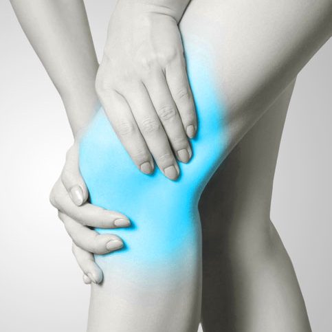 Closeup view of a young woman with knee pain on gray background. Black and white photo with blue dot.