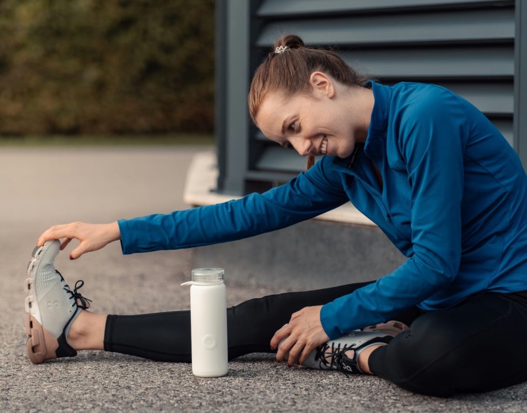 Woman stretching on the ground with a white water bottle in front of her