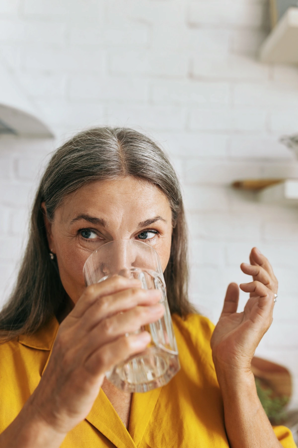 Cute middle-aged woman drinking water from glass. Mature female enjoying tasty beverage and looking away with gladness. Water balance, healthcare and healthy lifestyle concept